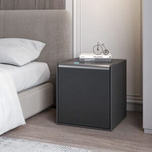 A black square box with a Burton Companion Fingerprint Safe on top of it next to a bed.